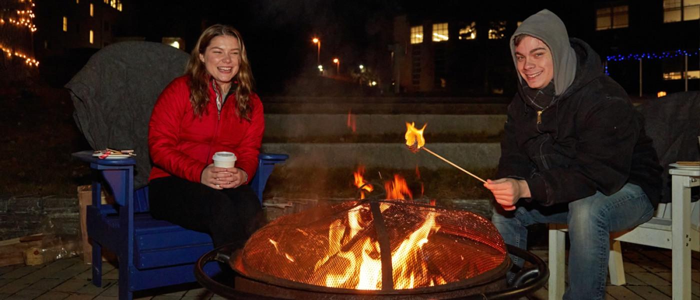 Students roast marshmallows and drink hot cocoa by a bonfire