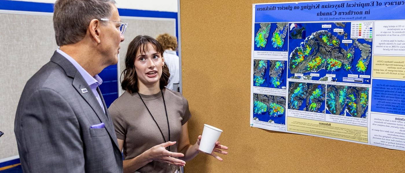A student talks about their research poster to President Herbert