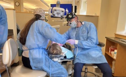 Two dental students clean a patient's teeth in the oral health clinic